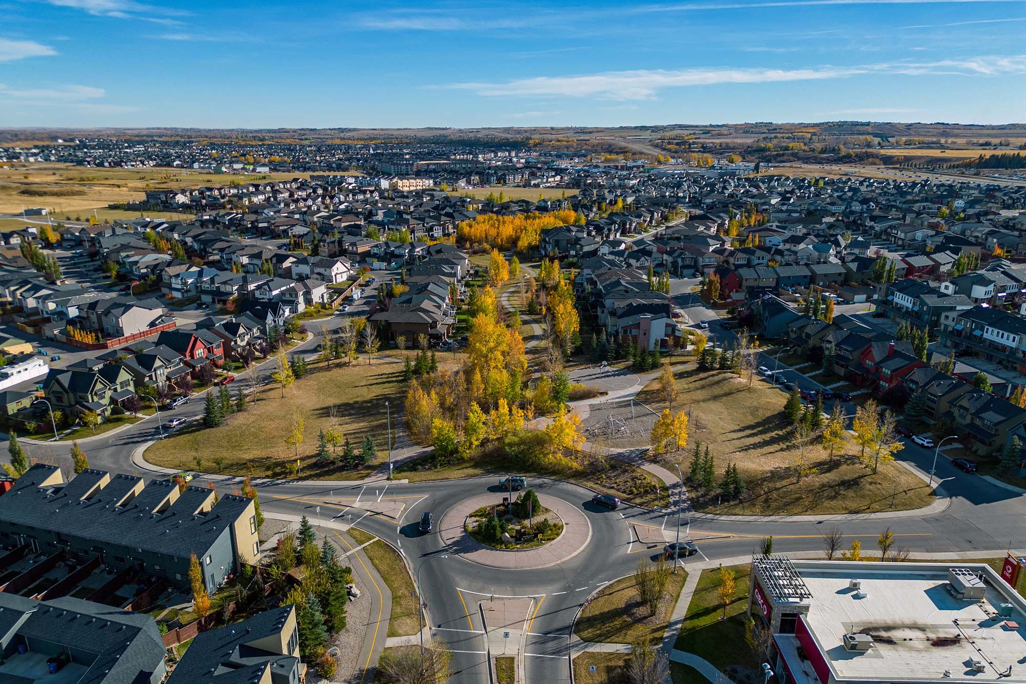 An south-facing aerial photograph of houses, streets, and tall trees in the community of Walden in Calgary, Alberta, Canada taken above the intersection of Walden Gate SE and Walden Dr SE.